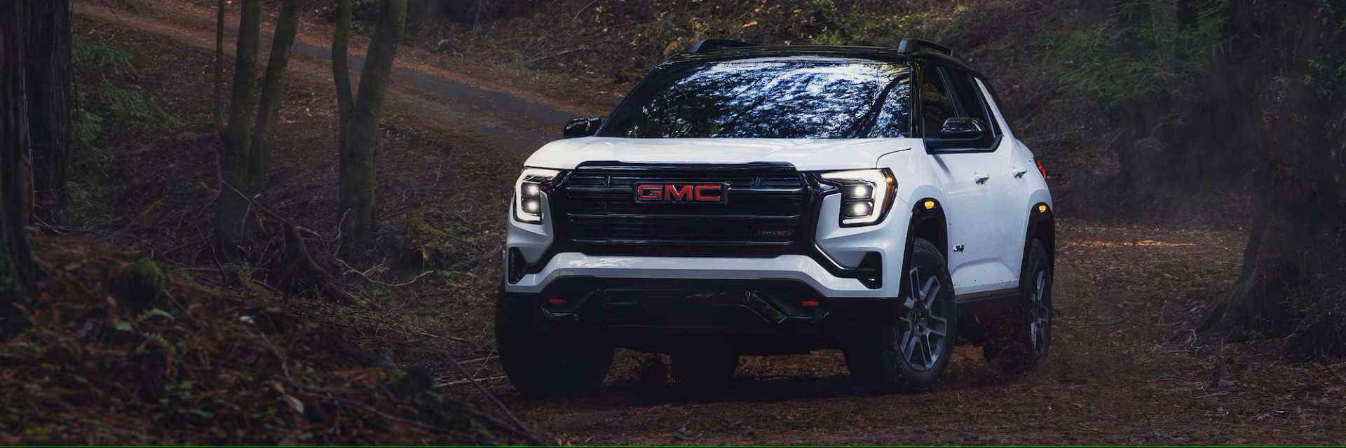 2026 GMC Terrain driving through a rugged forest trail, showcasing off-road capability and bold front-end styling.